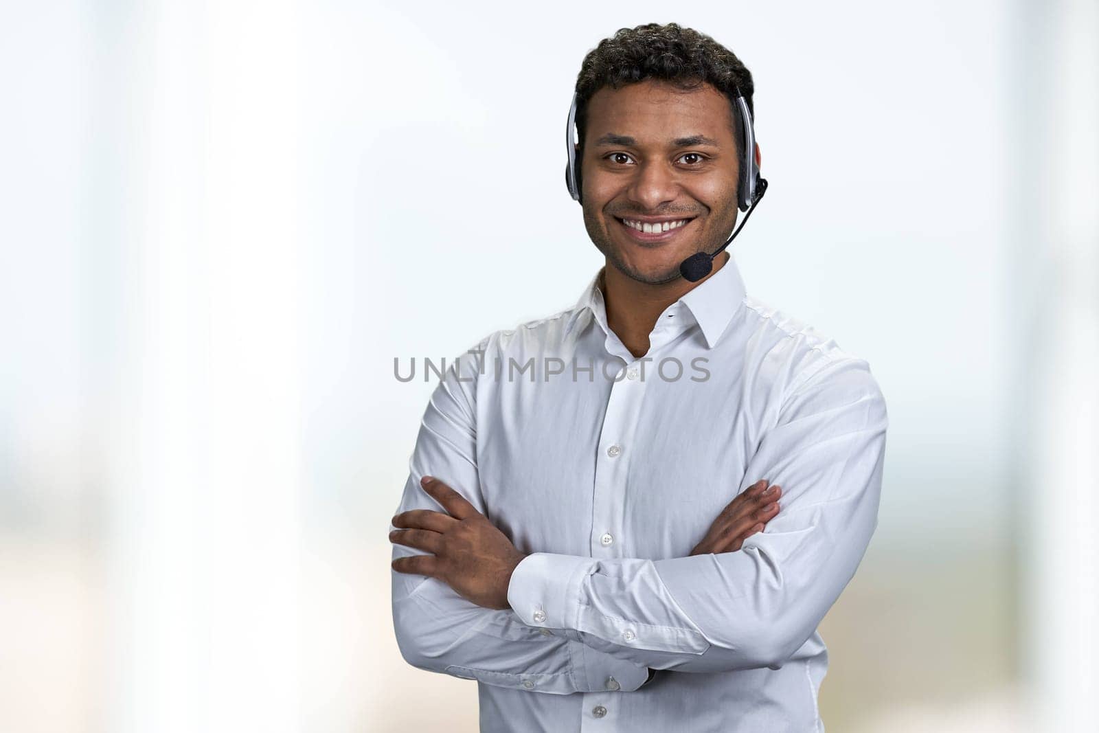 Portrait of male call center agent looking at camera with crossed arms. Call center operator on blurred background.