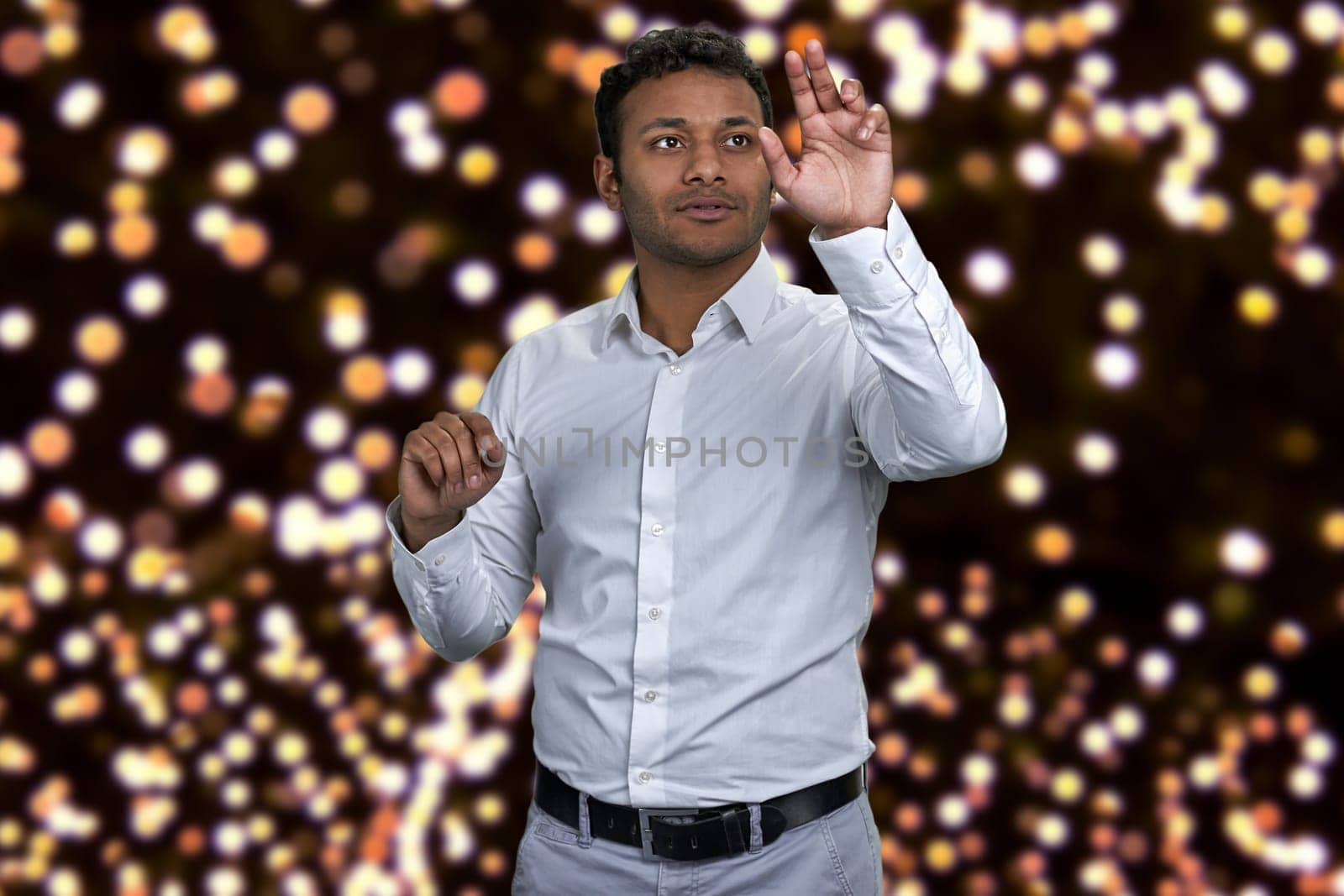 Young attractive indian businessman working on invisible interface. Festive bokeh lights in the background.
