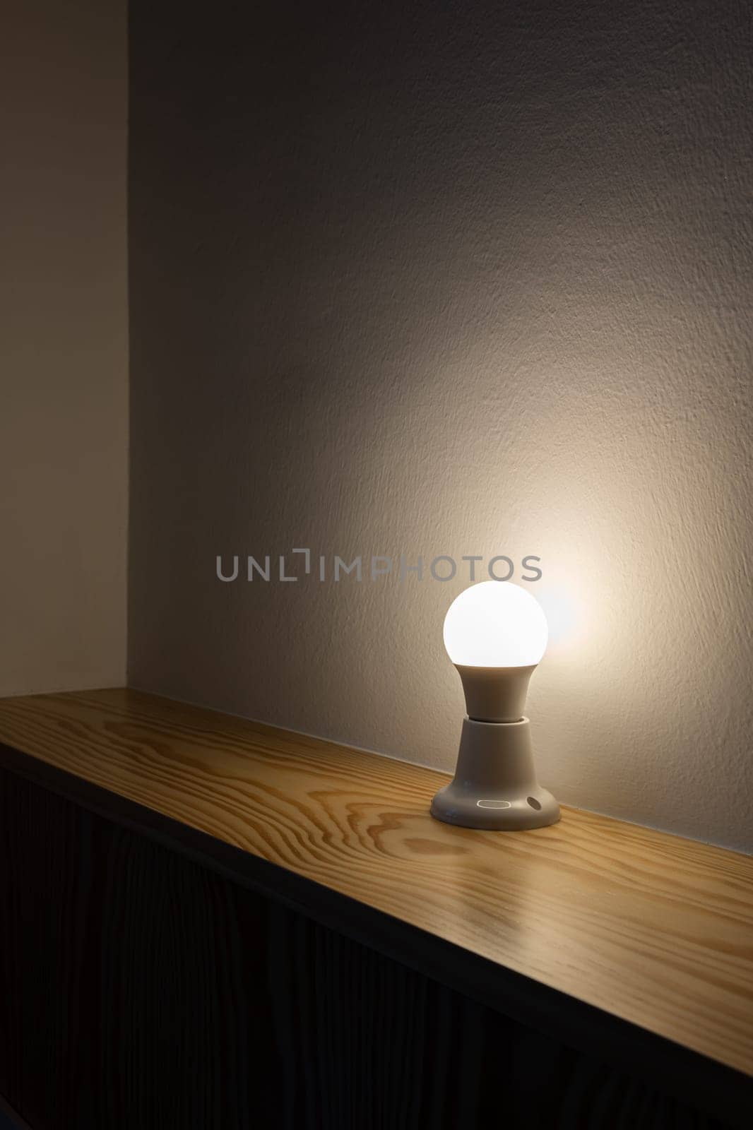 A light bulb on a wooden table in a dark room by apavlin