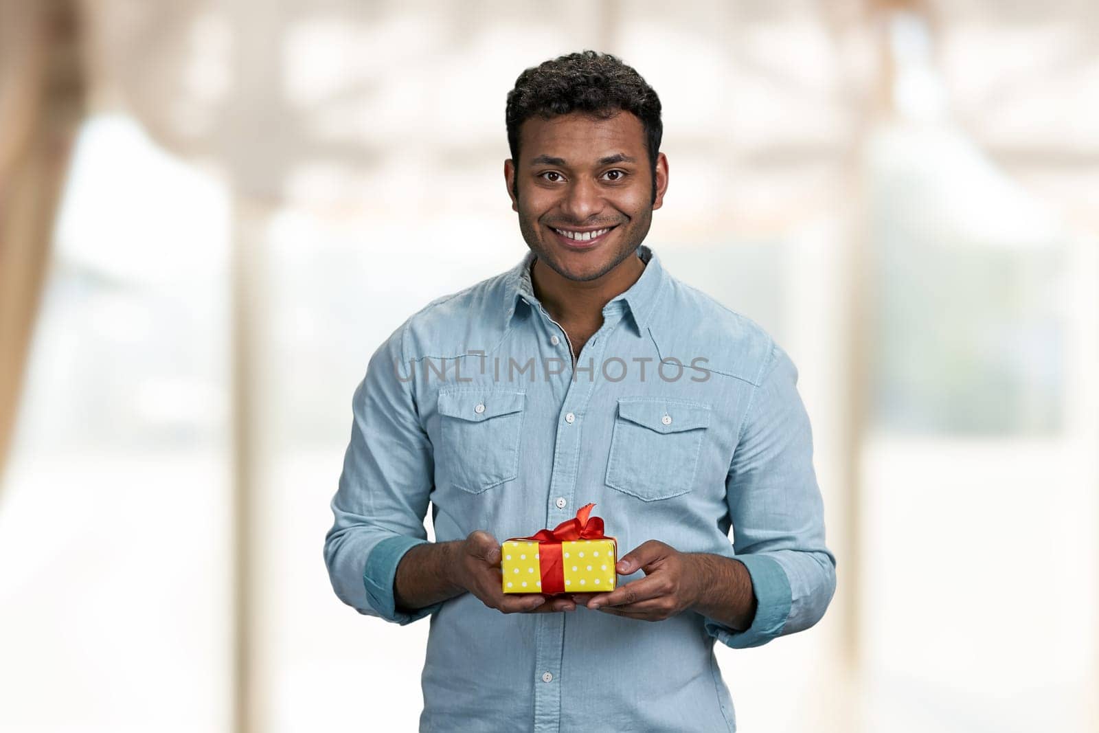 Handsome smiling man holding gift box and looking at camera. Birthday present for her.