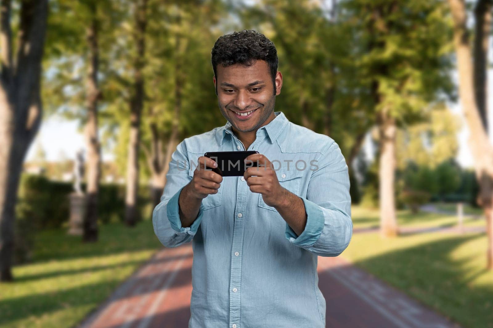 Cheerful young man using smartphone standing outdoors. People, technology and lifestyle concept.