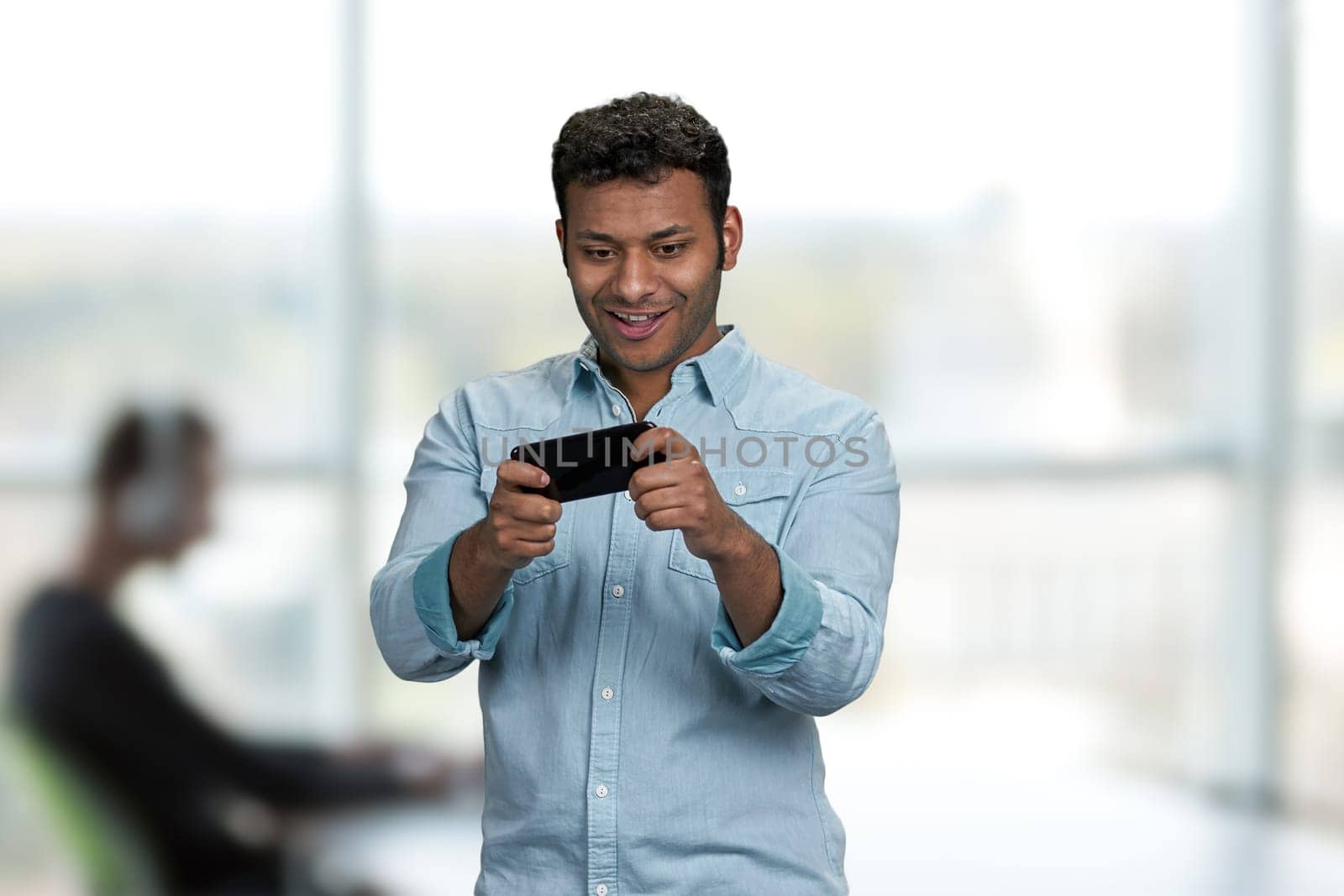 Young handsome man playing game on his smartphone. Office blur interior background.