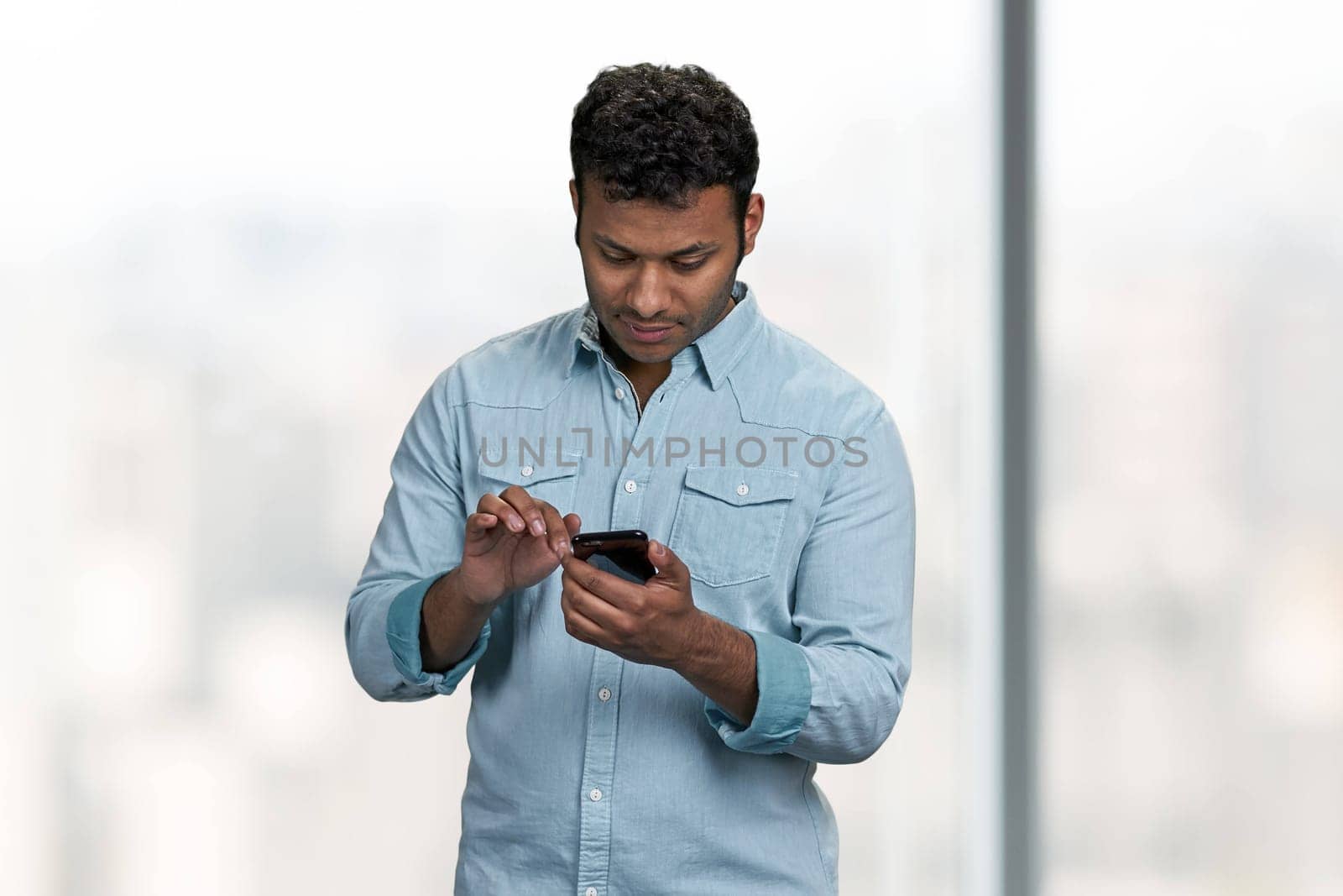 Young Indian man reading message on his mobile phone. Handsome guy using cell phone on blurred background.