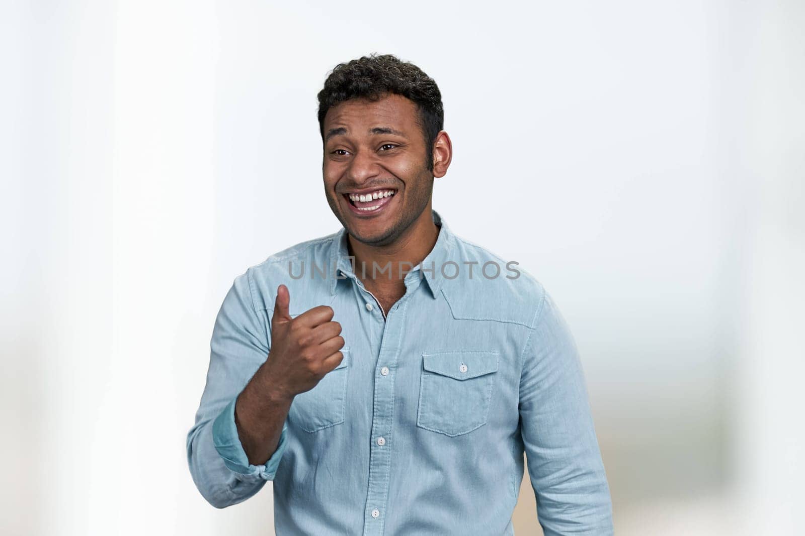 Young laughing man showing thumb up gesture standing on blurred background. Funny crazy joke. Human emotions and expressions.