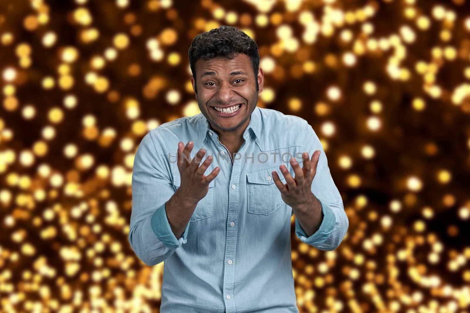 Happy cheerful young man expressing happiness on festive bokeh background. People, emotions and facial expression concept.