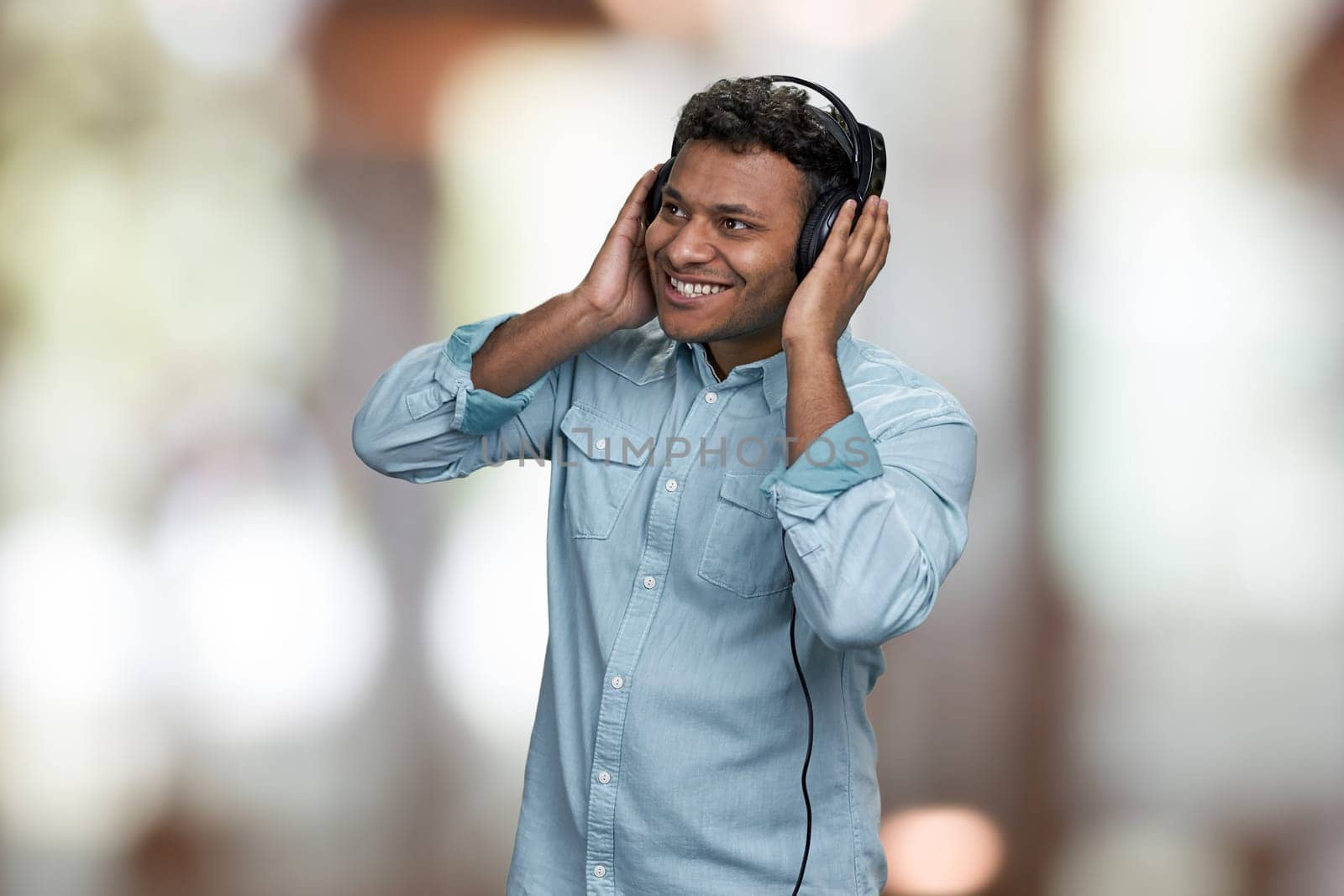 Cheerful young indian man listening music with headphones. Interior blur background. People, leisure and fun concept.