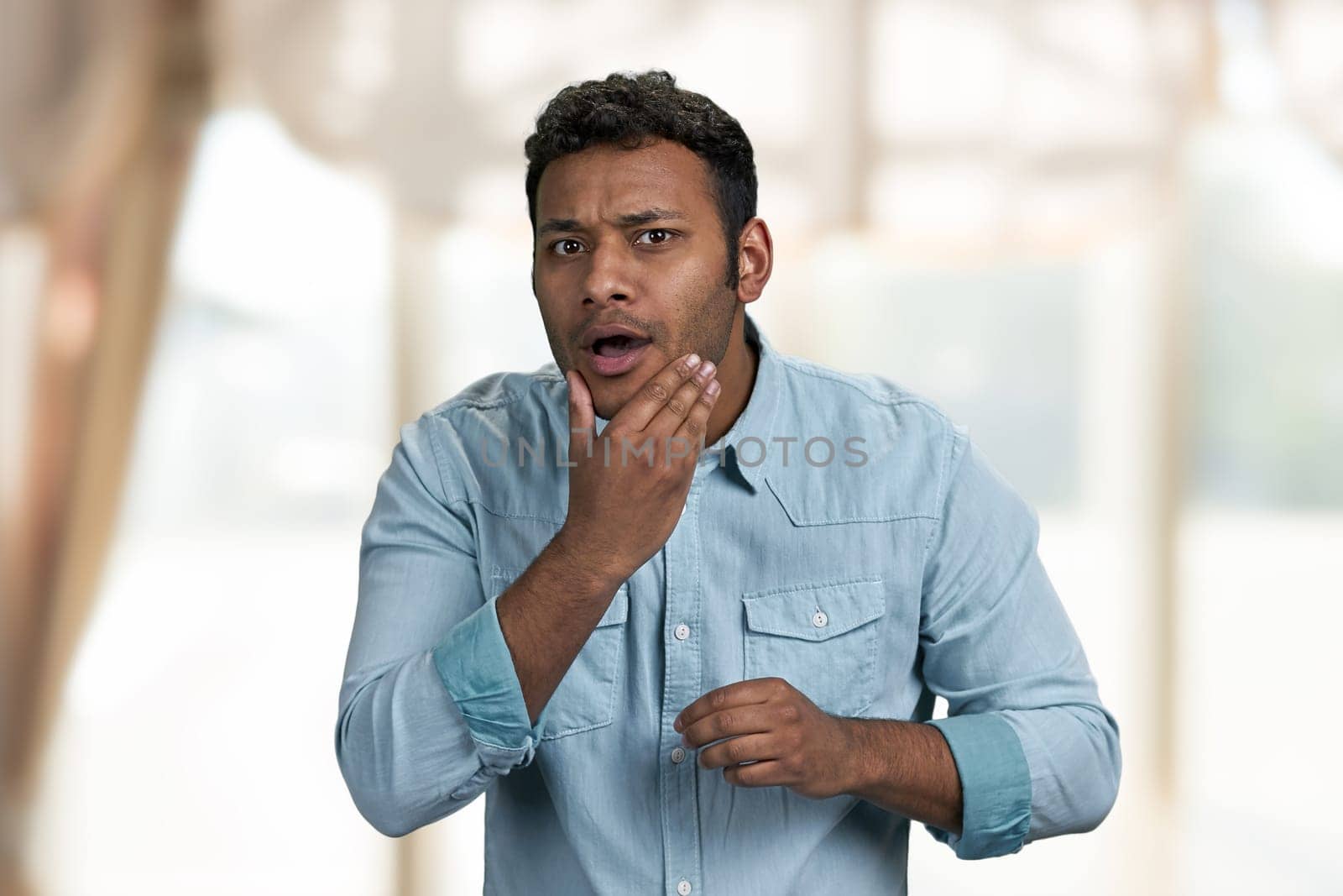 Young handsome indian man is preening before date. Blur interior background.