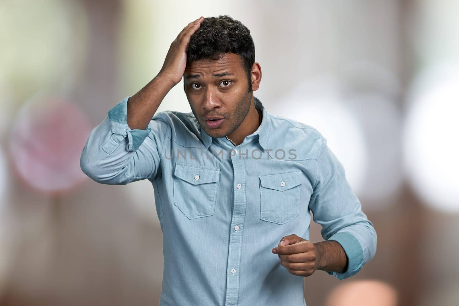 Sad young man touching his head because of headache. Abstract bokeh background.