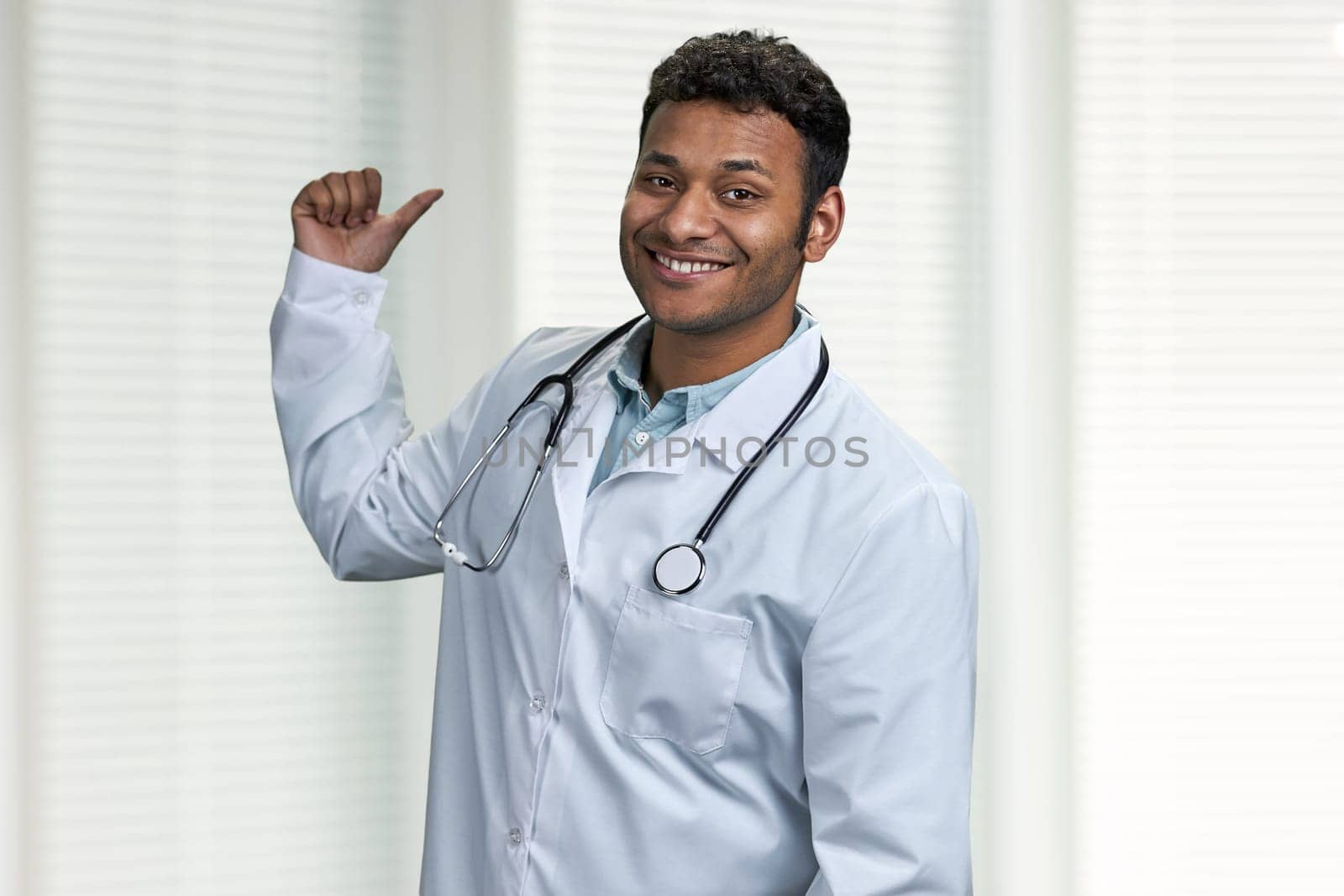 Smiling male doctor with stethoscope pointing with finger at copy space. Place for advertisement.