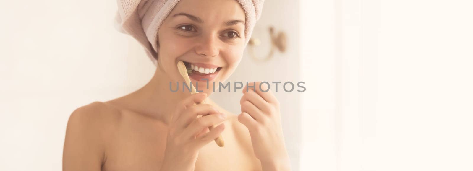 A young girl brushes her teeth near the mirror after relaxing in the bathroom, the woman is wrapped in a towel and takes care of the health and beauty of her body and teeth, gums.