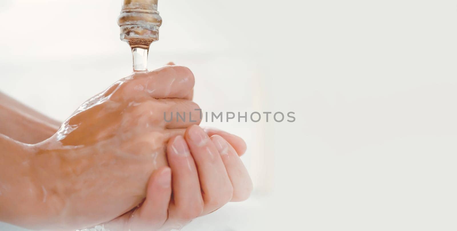 A young girl washes her hands thoroughly with soap under water in the bathroom, close-up view.