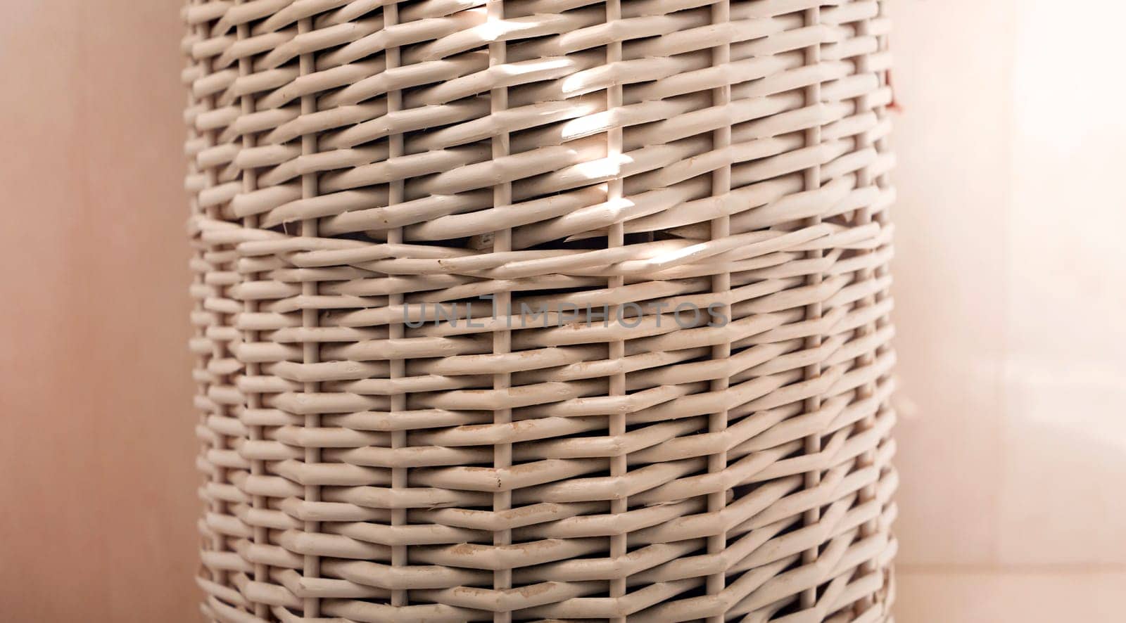 A white laundry basket, stylishly made of wicker wood, stands in the bathroom.