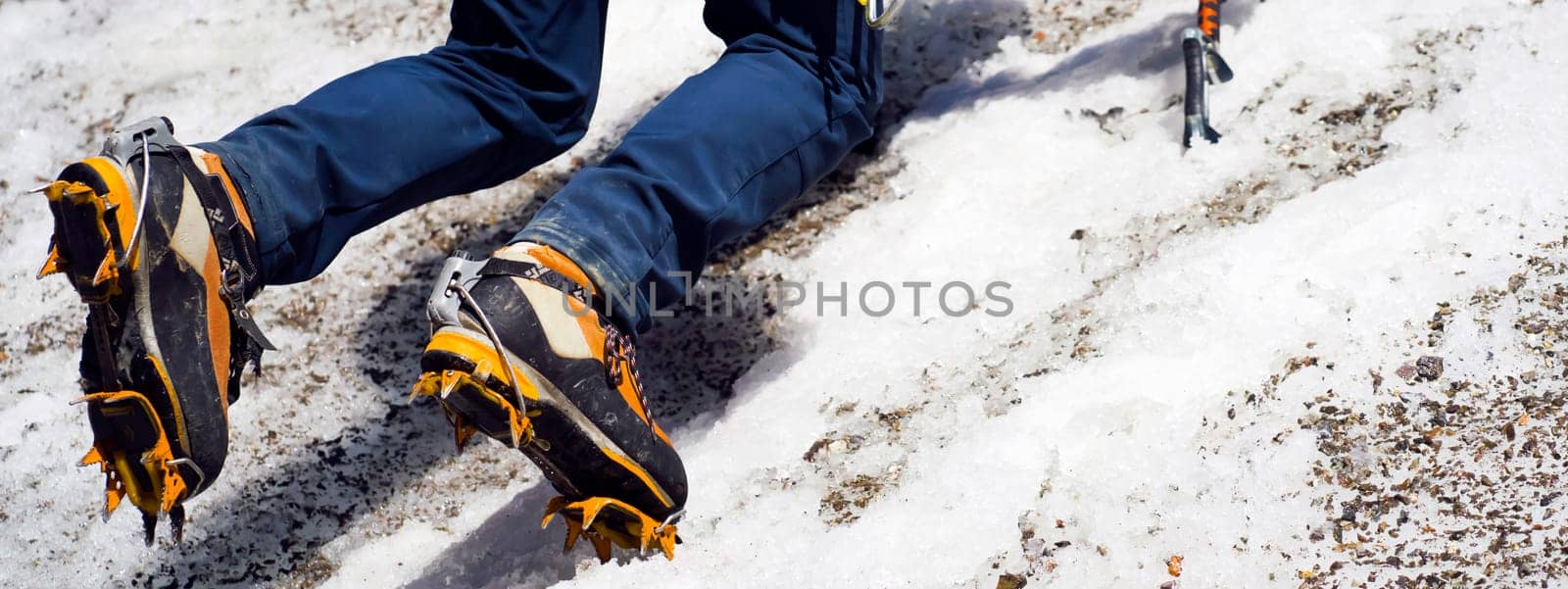 A man goes hiking, winter hiking in the highlands, and puts crampons on his climbing boots before climbing the glacier and snowy mountain.