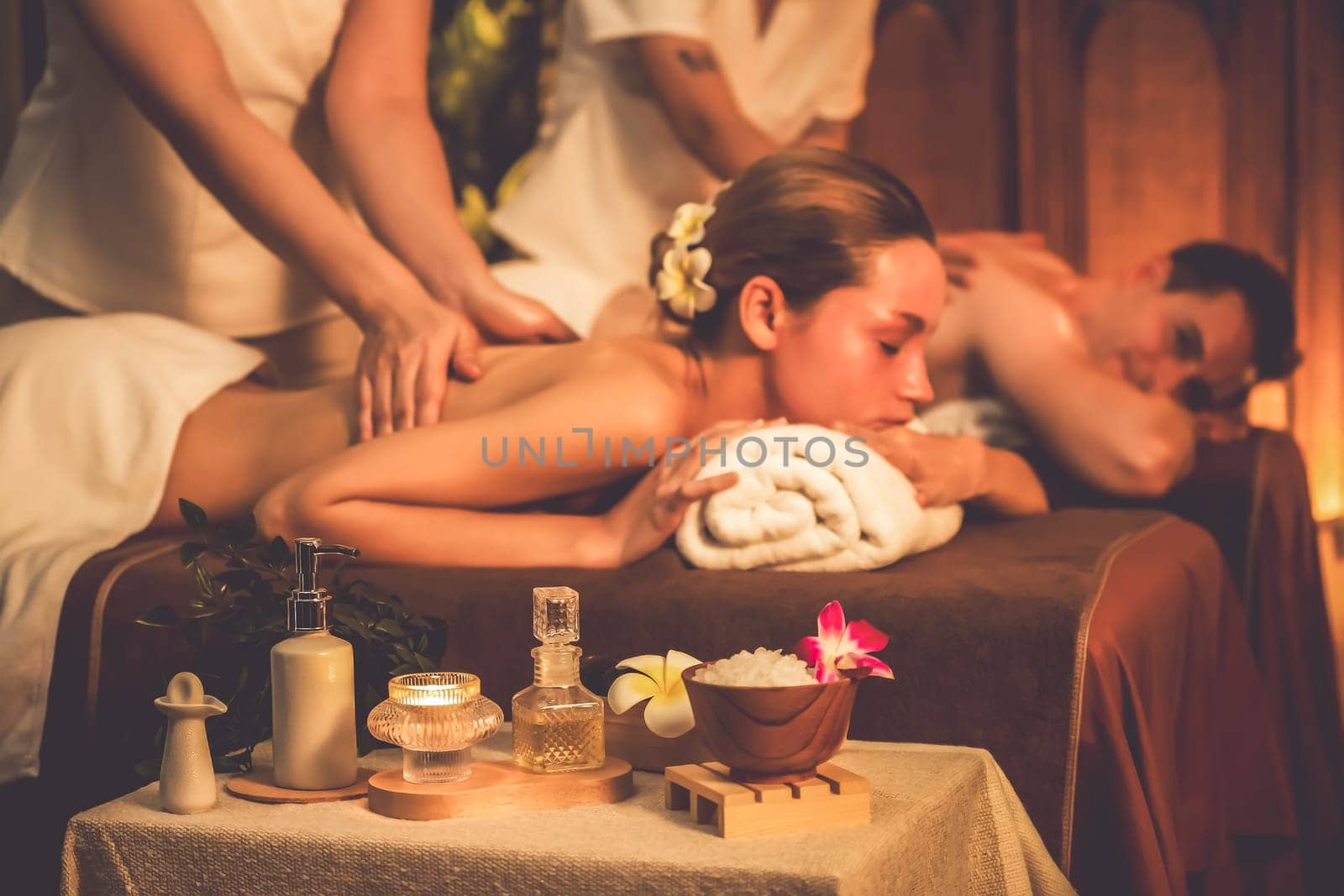 Caucasian couple customer enjoying relaxing anti-stress spa massage and pampering with beauty skin recreation leisure in warm candle lighting ambient salon spa at luxury resort or hotel. Quiescent