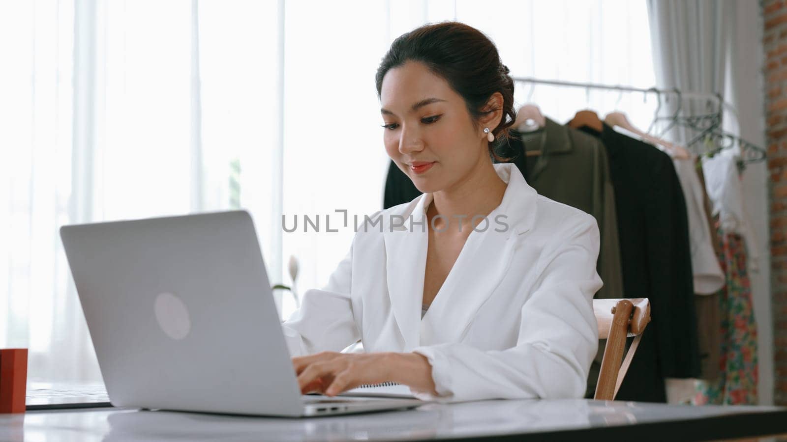 Young businesswoman sitting on the workspace desk using laptop computer for internet online content writing or remote working from home. Clothing and textile business marketing analysis. Vivancy