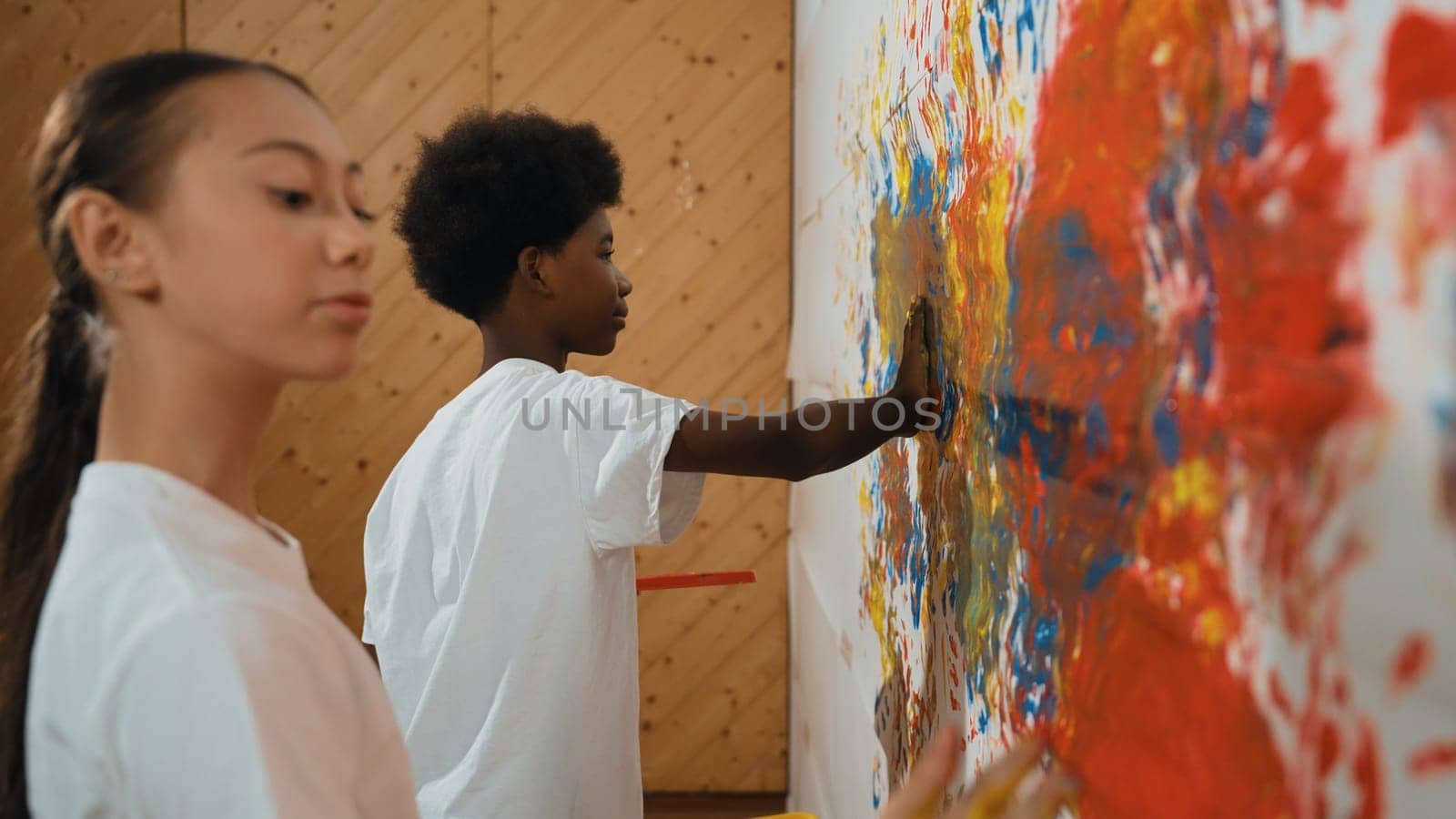 Diverse happy highschool girl and african boy paint the wall with water color in red and blue or contrast color by using their hands in art lesson. Side view. Creative activity concept. Edification.