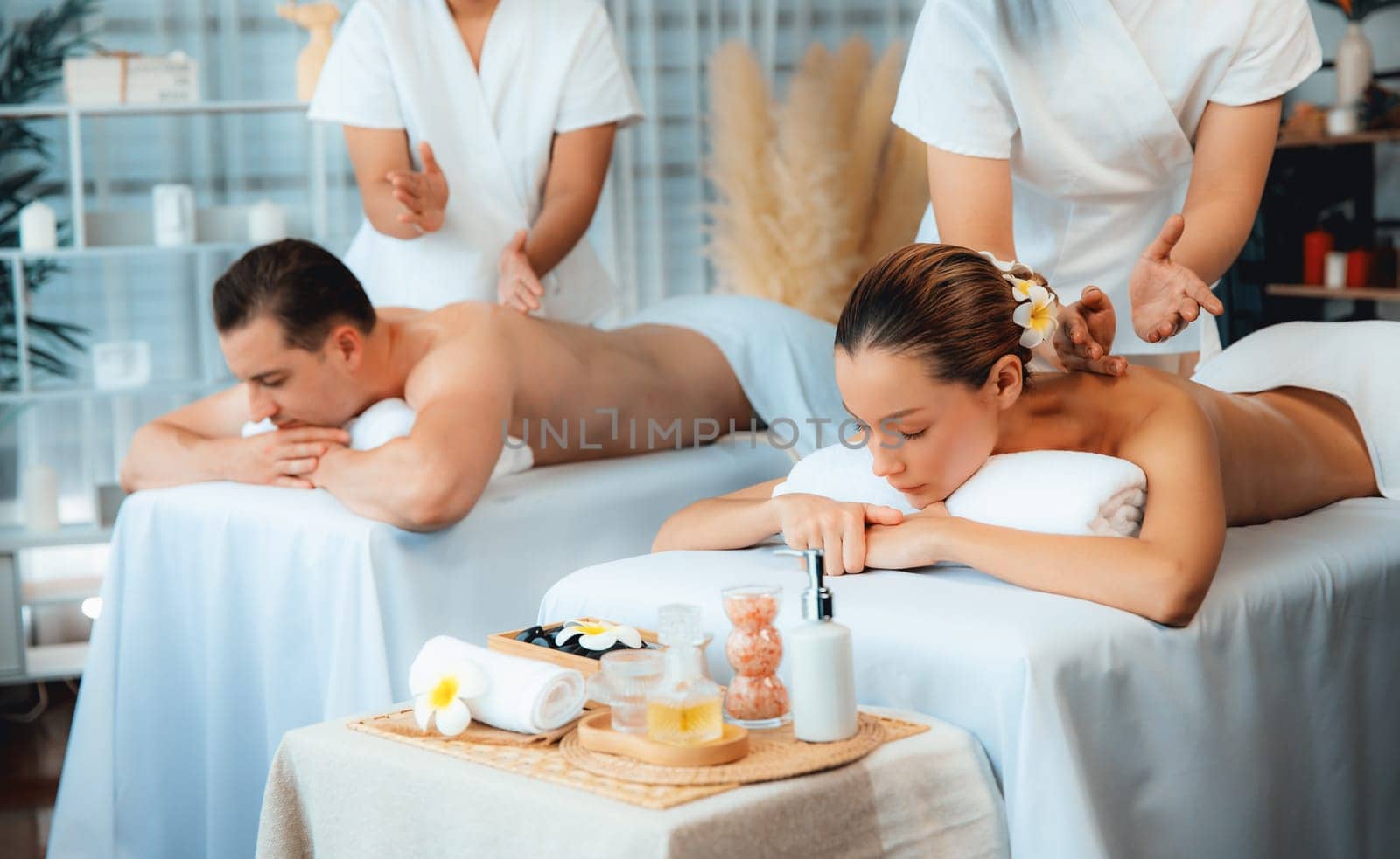 Caucasian couple customer enjoying relaxing anti-stress spa massage and pampering with beauty skin recreation leisure in day light ambient salon spa at luxury resort or hotel. Quiescent