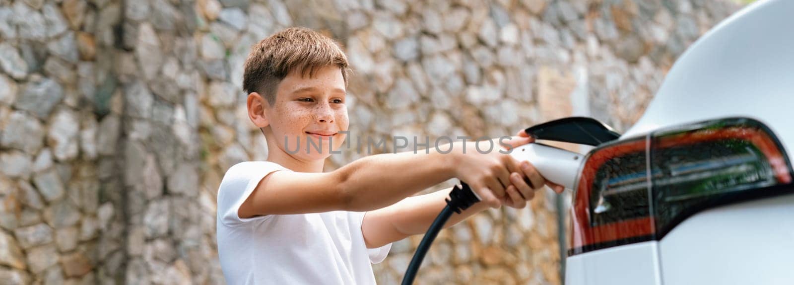 Little boy recharging eco-friendly electric car from EV charging station. EV car road trip travel concept for alternative transportation powered by clean renewable and sustainable energy. Perpetual