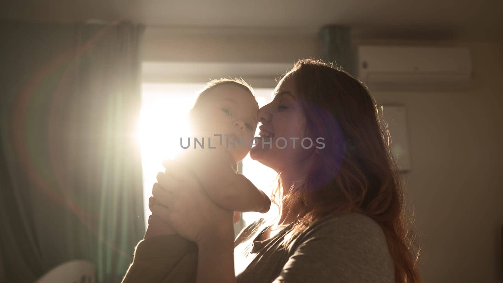 A Caucasian woman tenderly kisses her newborn son in the morning rays of sunlight. by mrwed54