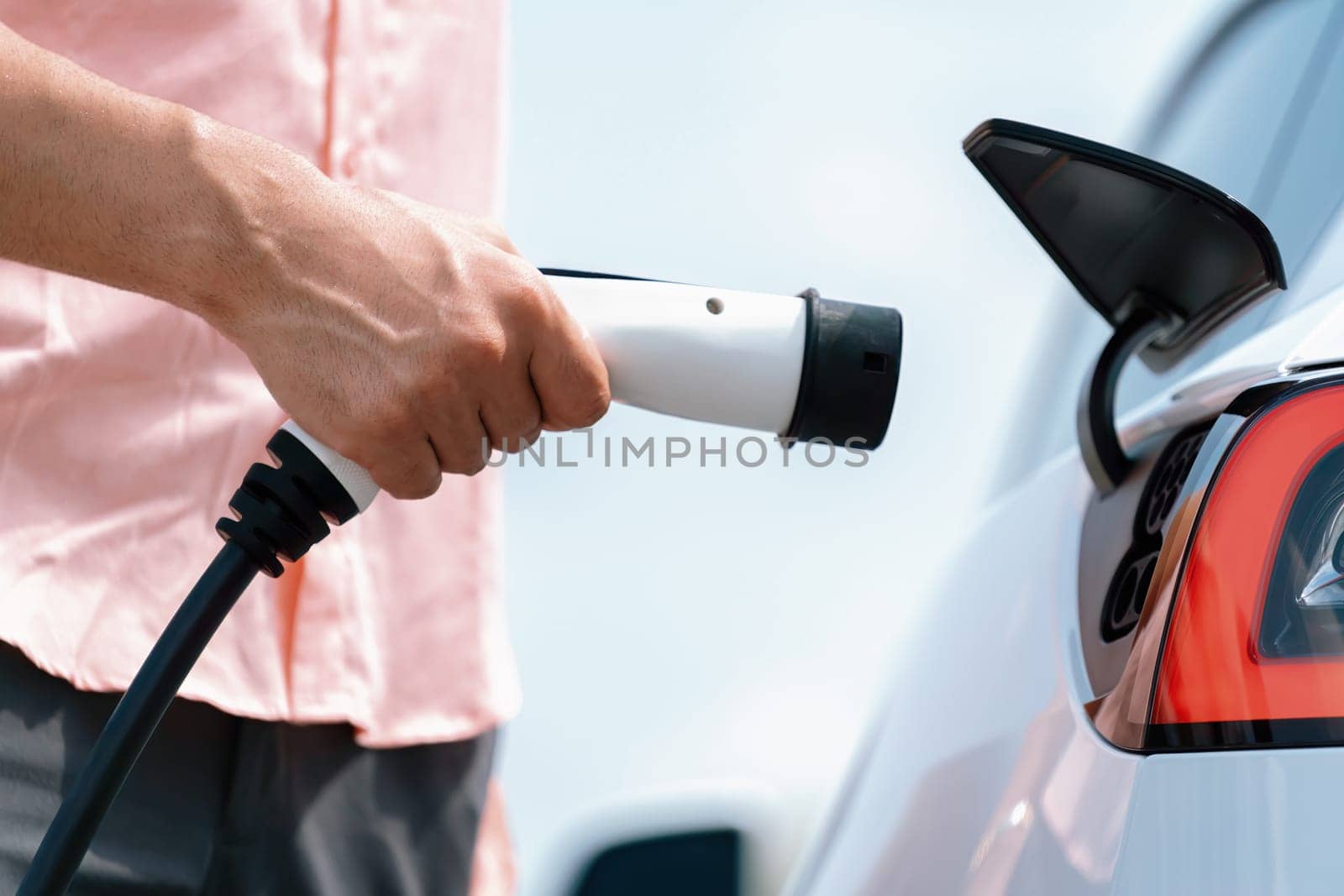 Hand insert EV charger plug into electric vehicle to recharge EV car. Perpetual by biancoblue