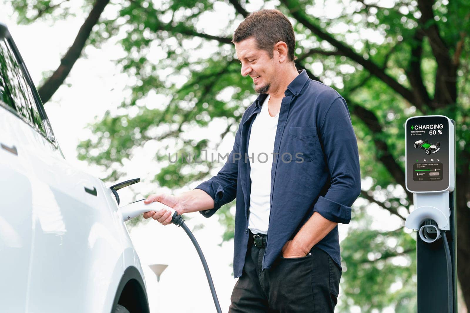 Man recharging battery for electric car during road trip travel EV car in natural forest or national park. Eco friendly travel during vacation and holiday. Exalt