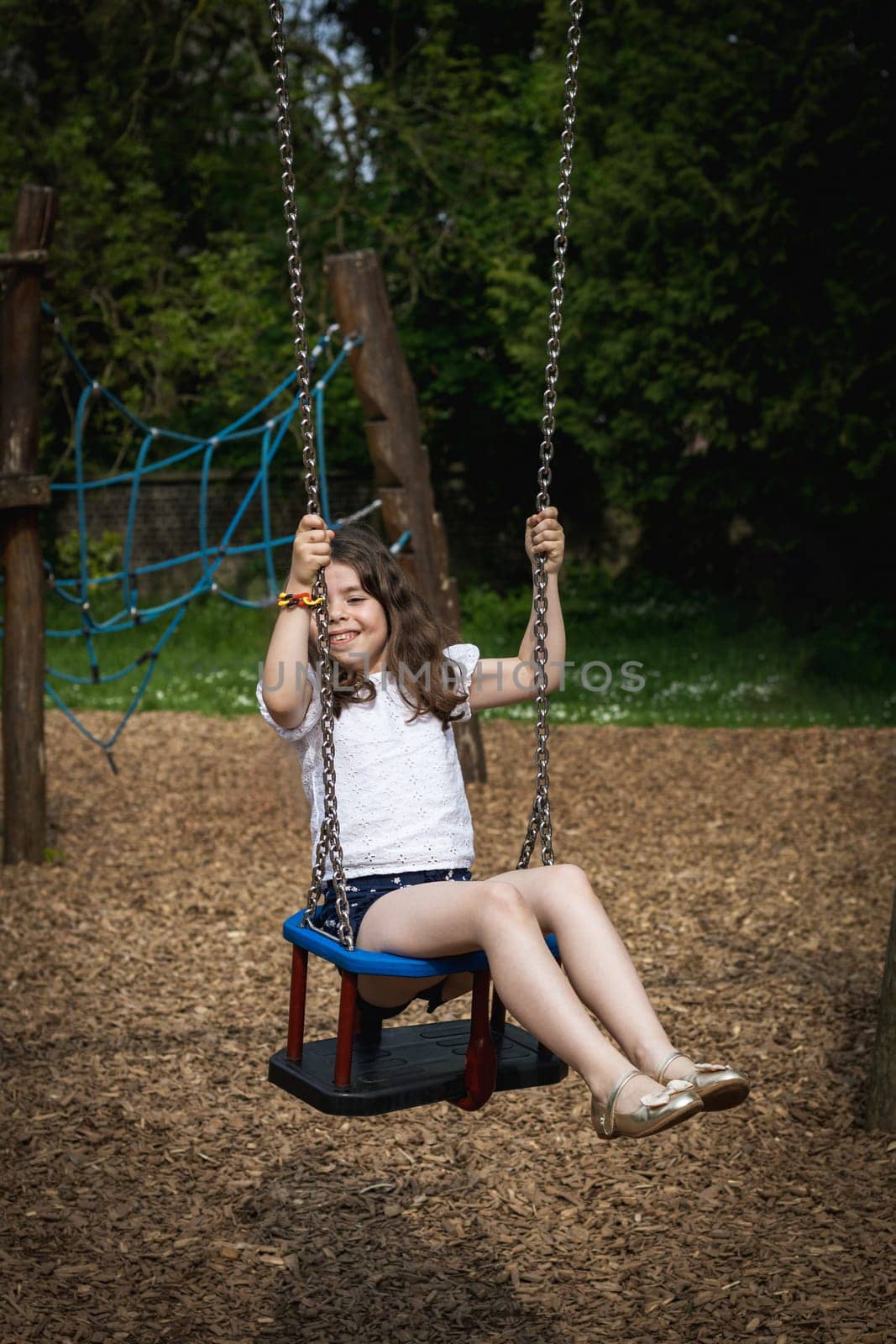 Portrait of a happy girl riding on a swing. by Nataliya
