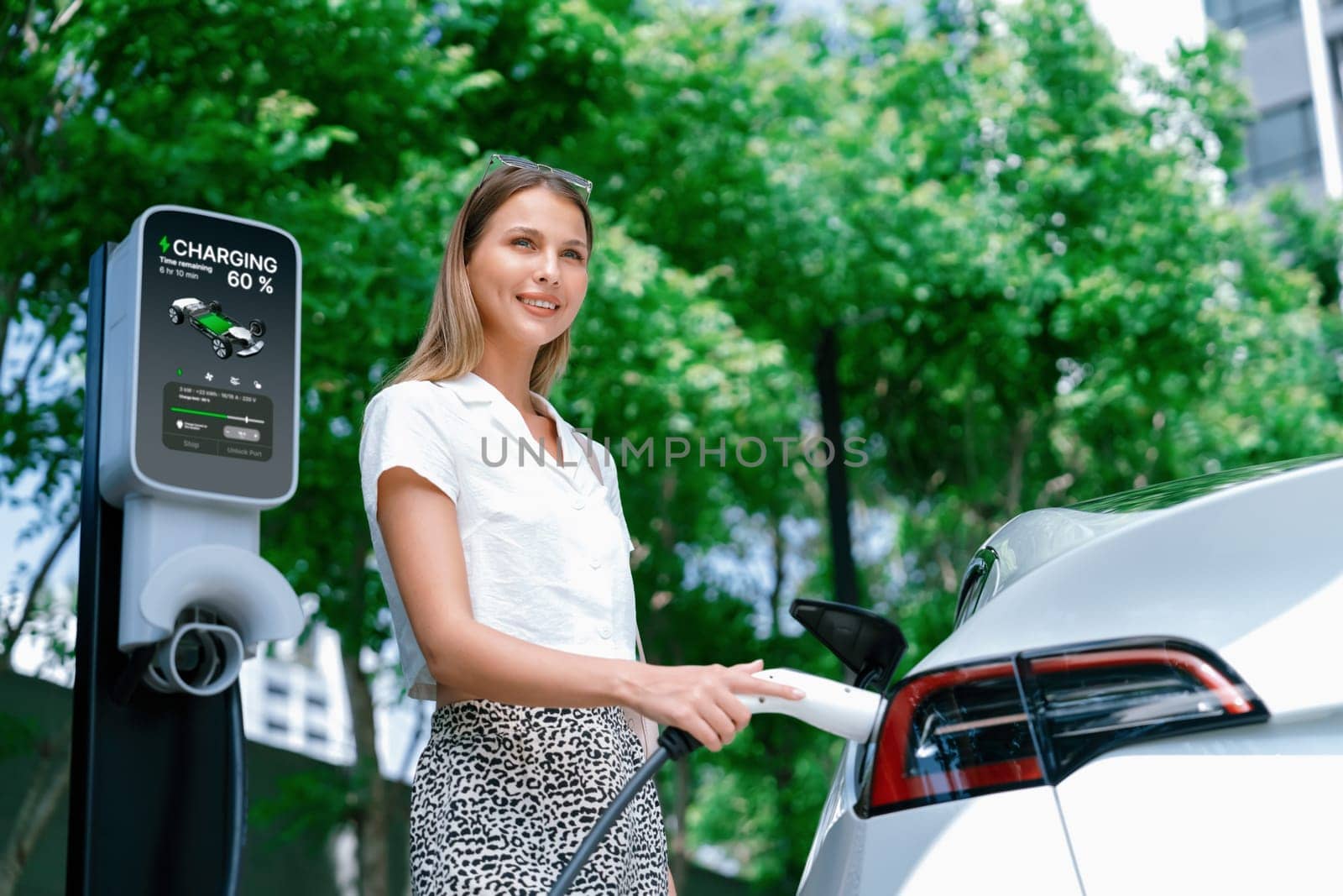 Young woman travel with EV electric car charging in green sustainable city outdoor garden in summer. Urban sustainability lifestyle by green clean rechargeable energy of electric BEV vehicle innards