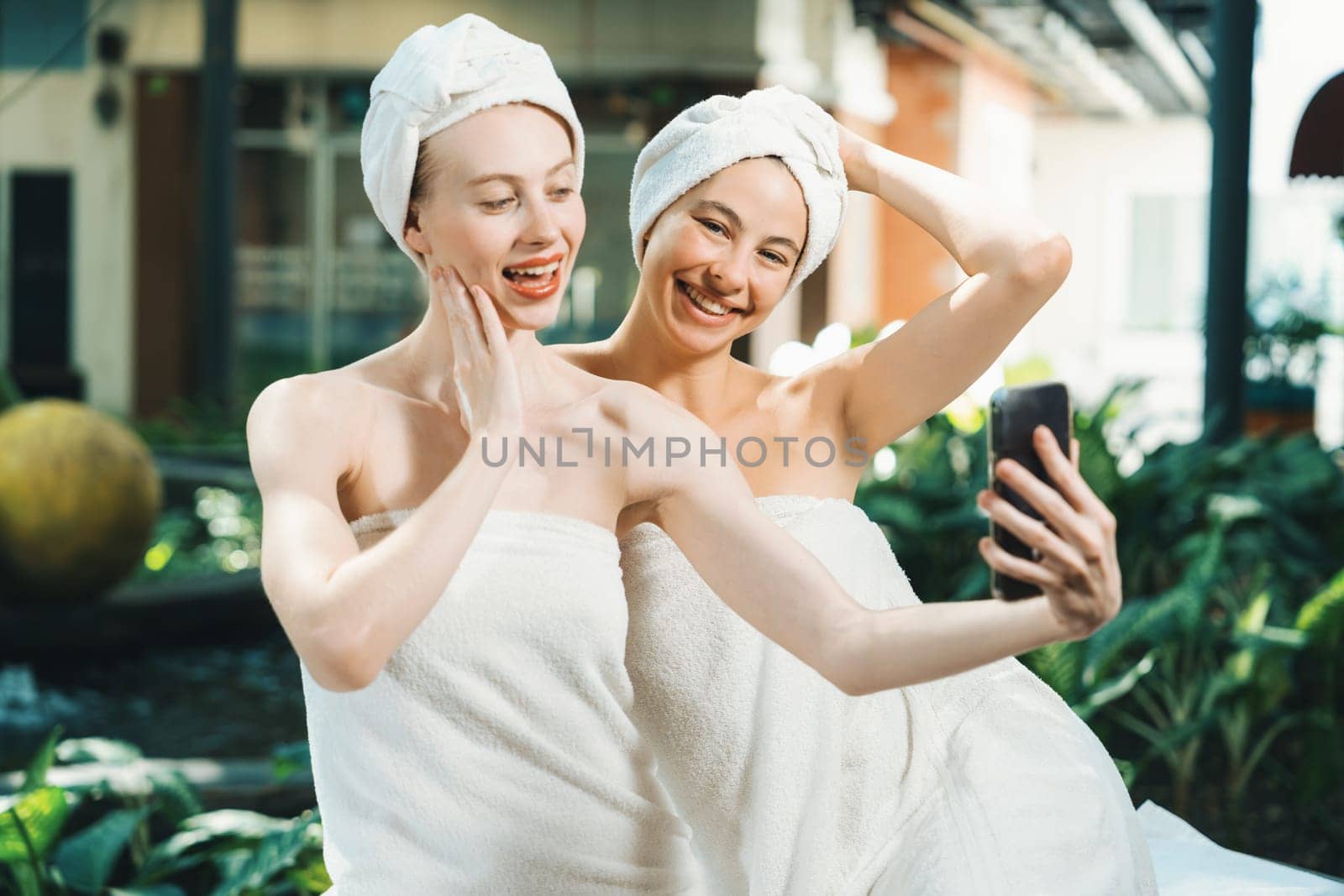 Couple of young beautiful women with beautiful skin in white towel taking a photo together at outdoor surrounded by peaceful natural environment. Beauty and healthy spa concept. Tranquility.