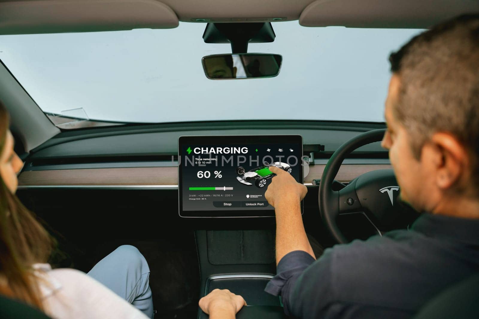 Two lovely couple inside the vehicle, checking battery recharging electricity status display on smart monitor screen in modern EV car on their road trip journey. Exalt