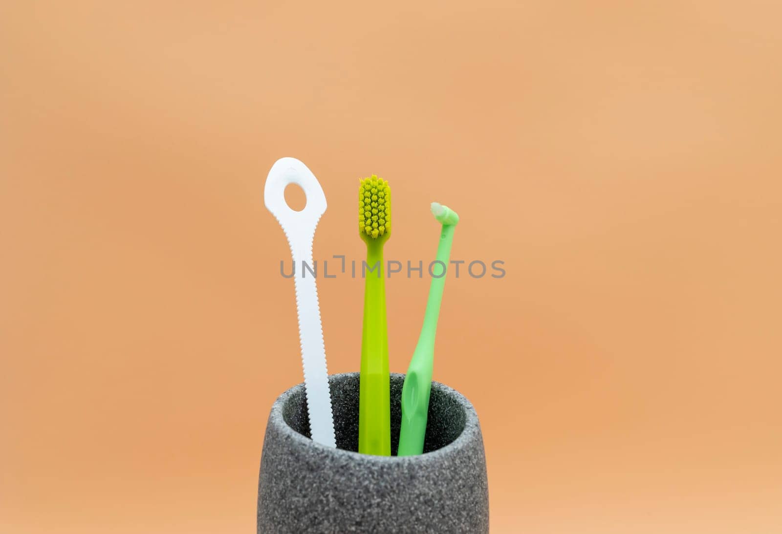 Personal Dental Oral Hygiene Set. Green Toothbrush, White Flexible Tongue Scraper, Interdental Toothbrush For Cleaning Between Teeth On Peach Yellow Background. Space For Text. Horizontal Plane. by netatsi