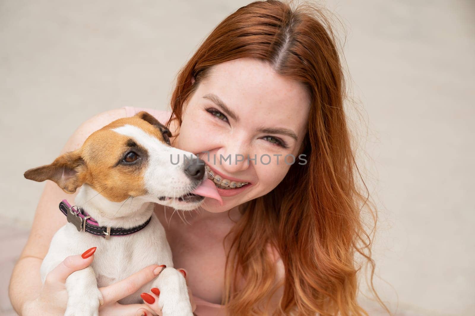 Dog jack russell terrier licks the owner in the face outdoors. Girl with braces on her teeth. by mrwed54
