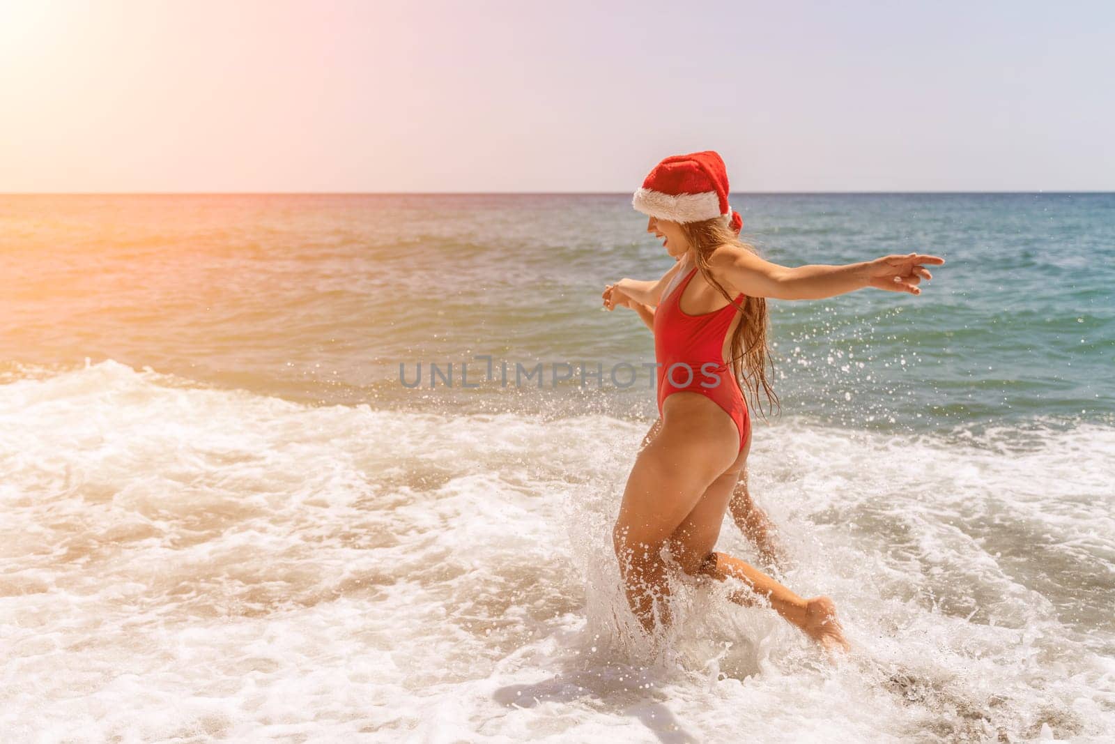 Women in Santa Claus hats run into the sea dressed in red swimsuits. Celebrating the New Year in a hot country by Matiunina