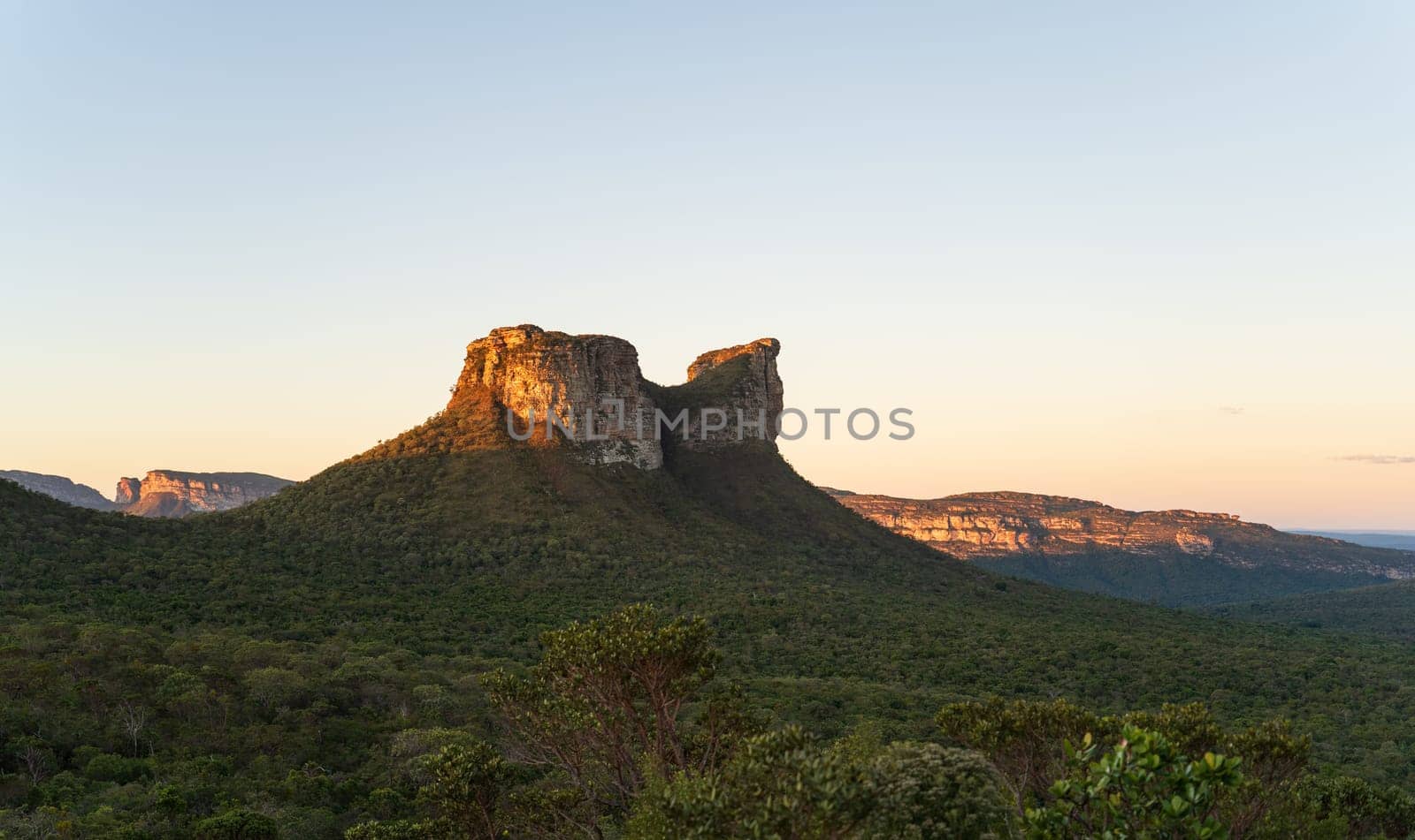 Breathtaking sunset at Chapada Diamantina, Brazil with a camel-shaped rock rising above a lush landscape under a clear sky. Ideal for text placement.