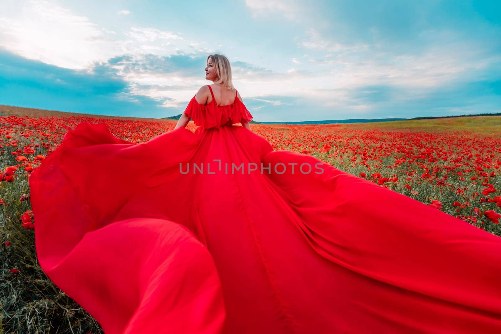 Woman poppy field red dress. Happy woman in a long red dress in a beautiful large poppy field. Blond stands with her back posing on a large field of red poppie