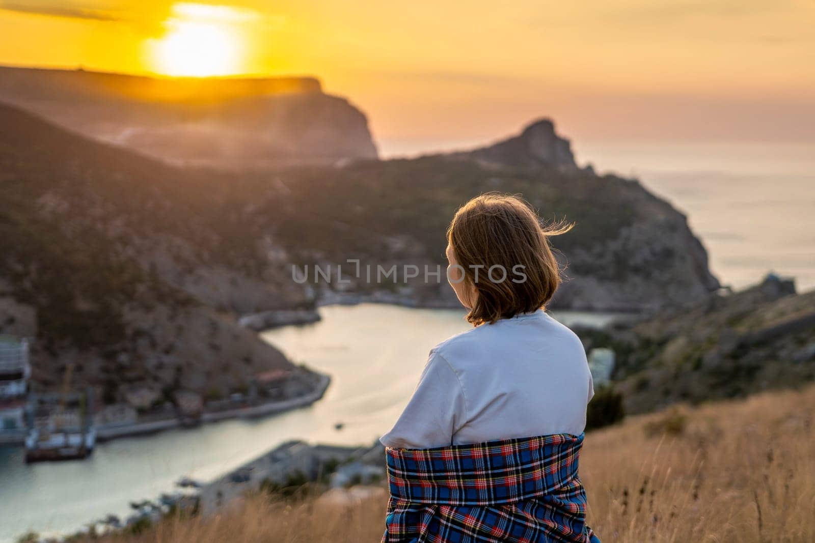 Happy woman on sunset in mountains. Woman siting with her back on the sunset in nature in summer. Silhouette. by Matiunina