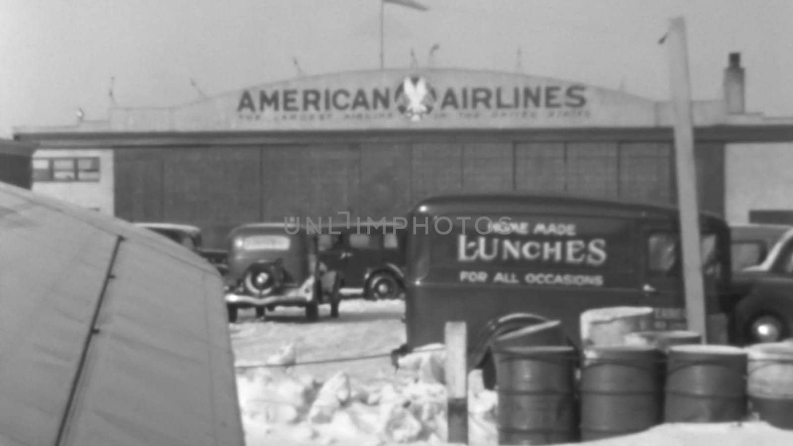 Unique perspective from inside a 1930s airliner. Photo shows airport hangars, other structures, and fuel drums on the tarmac, captured through the airplane window. Boeing 247 of United Air Lines