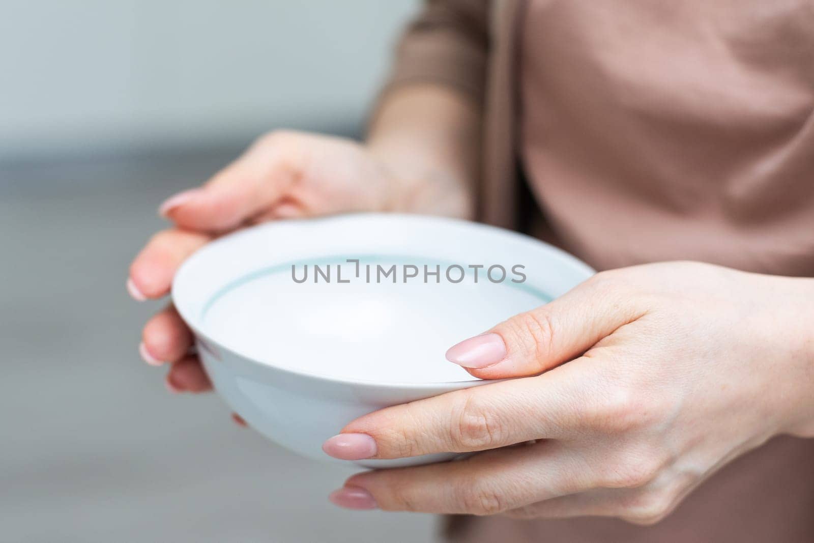 Unrecognizable woman holding empty bowl in her hands, kitchen interior, copy space, closeup shot, cropped of hungry lady starving. Famine, poverty, hunger, crisis concept. High quality photo