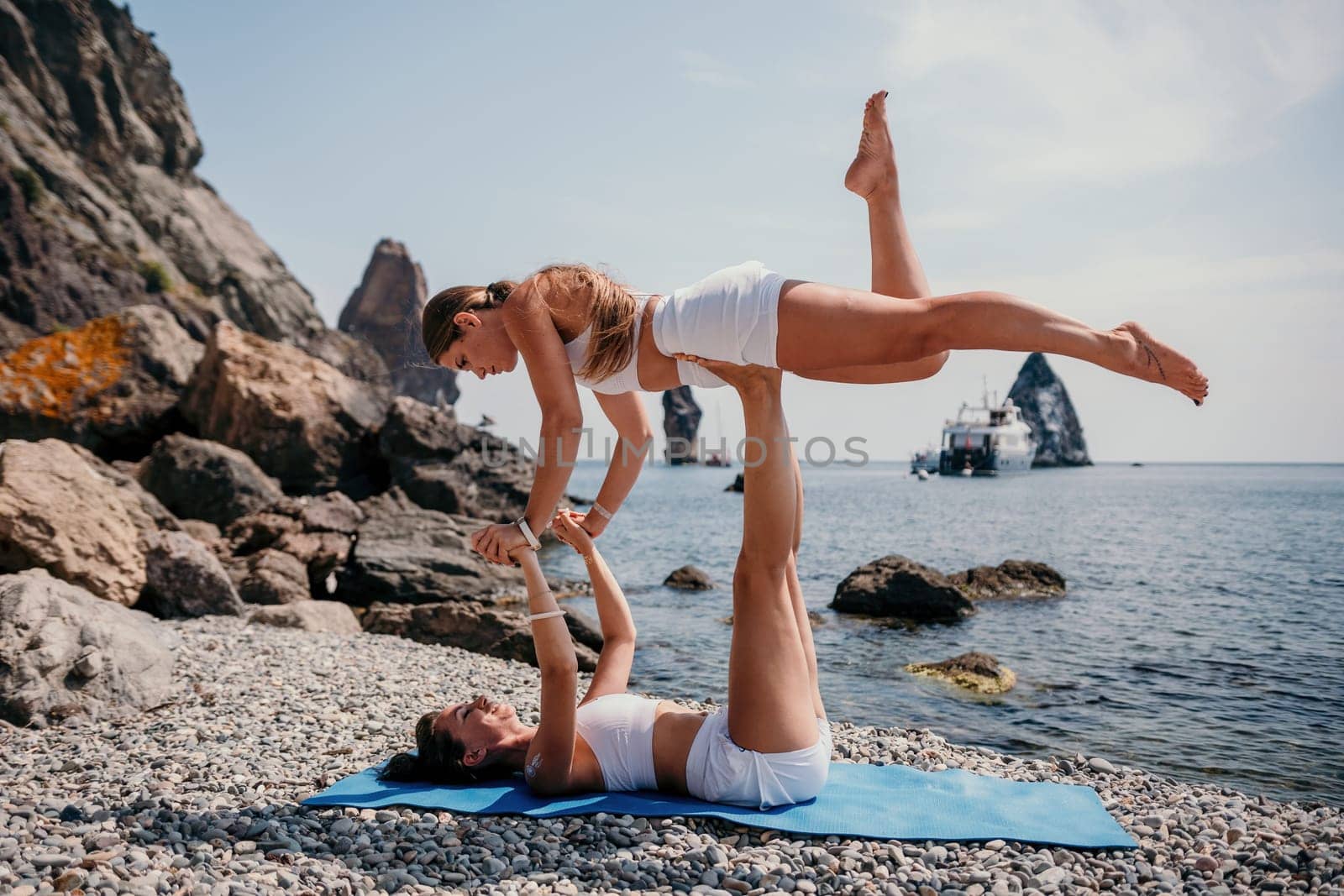 Woman sea yoga. Two Happy women meditating in yoga pose on the beach, ocean and rock mountains. Motivation and inspirational fit and exercising. Healthy lifestyle outdoors in nature, fitness concept. by panophotograph