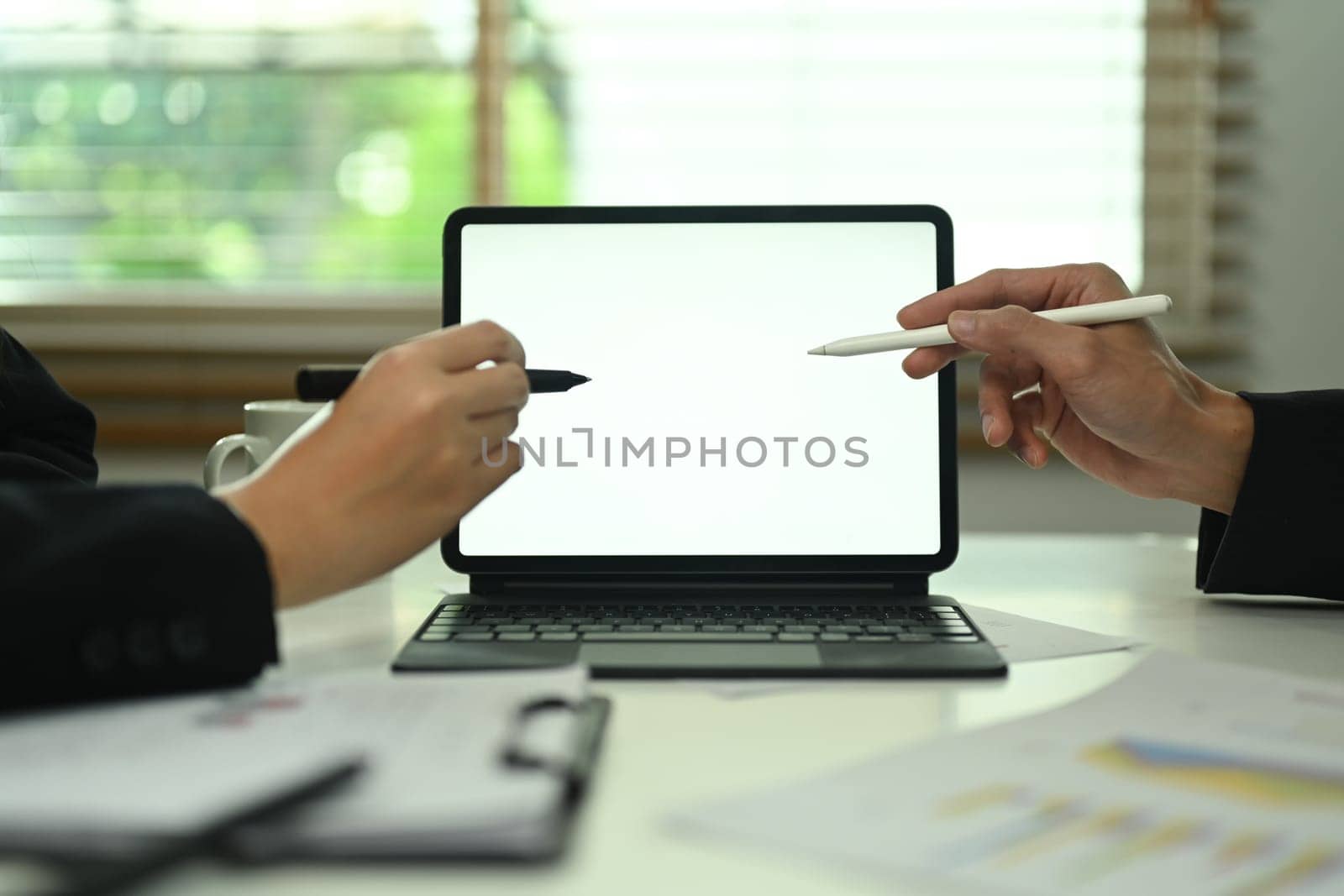 Cropped shot businesspeople pointing at digital tablet, discussing financial plan at office.