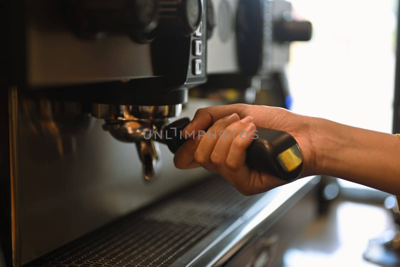 Cropped shot of barista using coffee machine, making espresso for client in a trendy cafe.