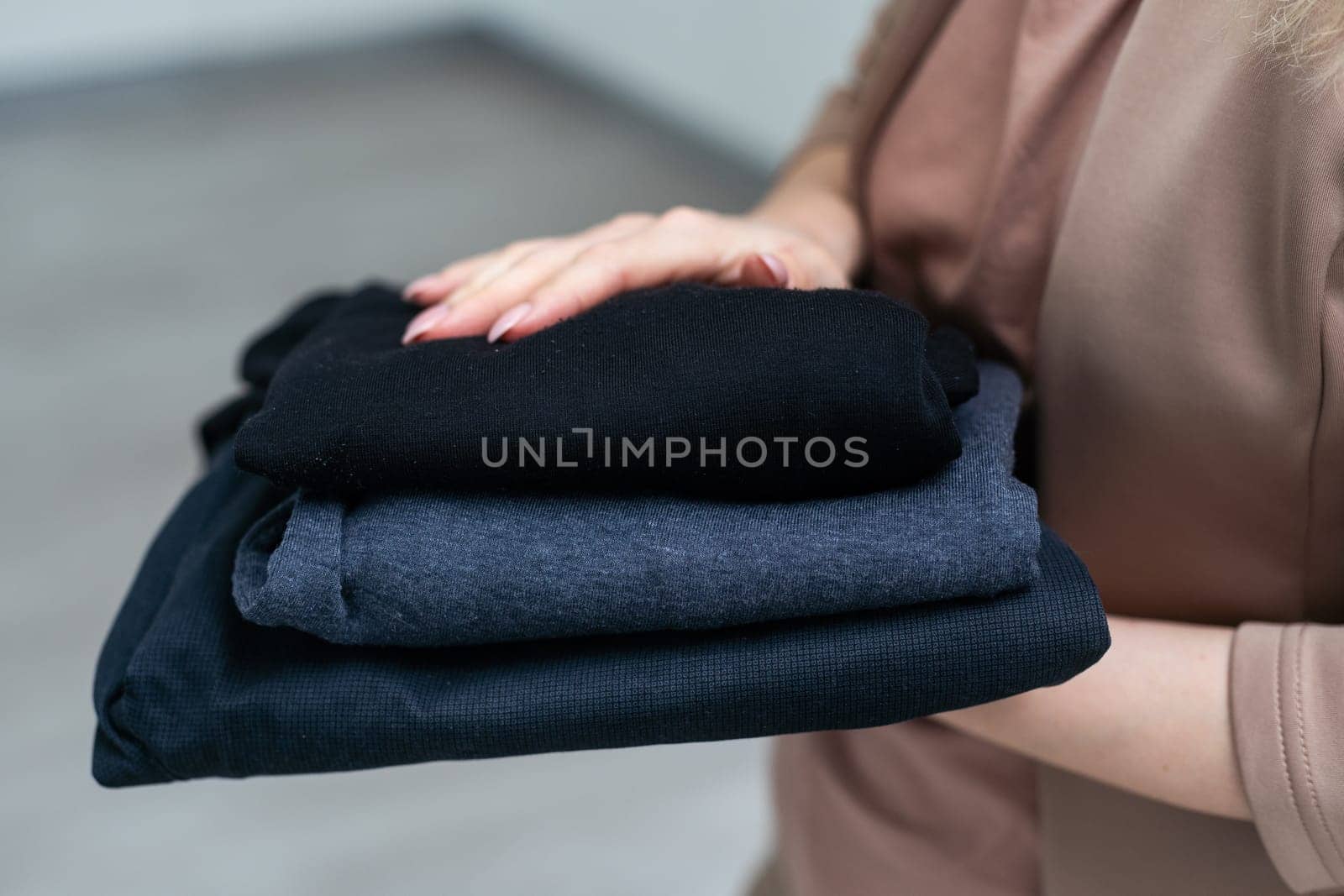 Hand holding basic t-shirts of different colors against grey background. Casual clothes for men or women, fashion concept. High quality photo