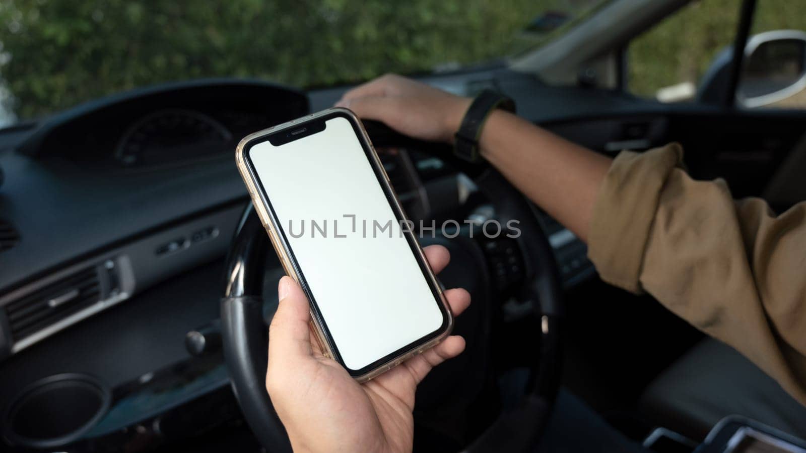 Cropped shot of man sitting behind wheel of a car and using smartphone. Closeup view.