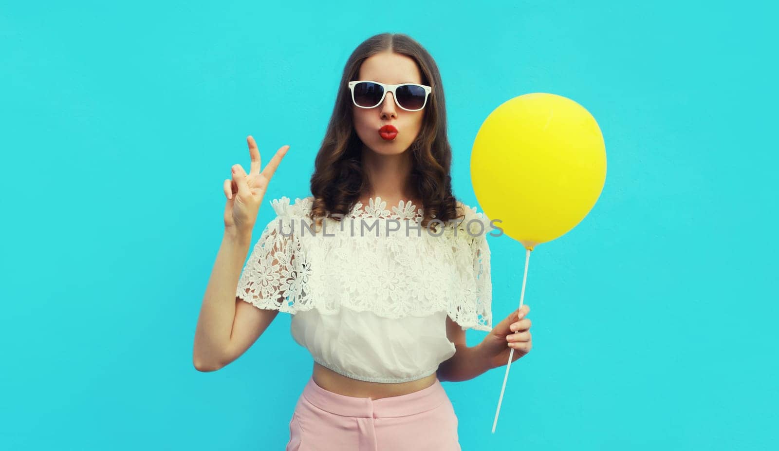 Portrait of happy young woman with yellow balloon on blue studio background