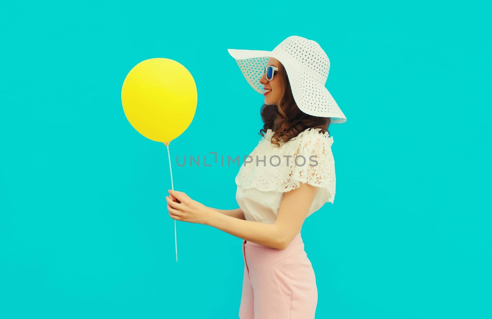 Portrait of happy young woman with yellow balloon on blue studio background