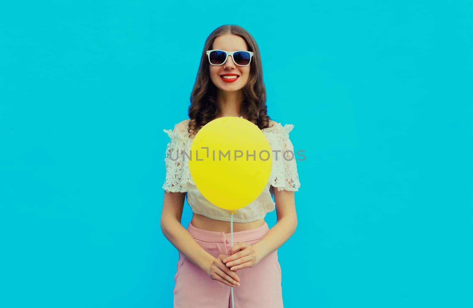 Portrait of happy young woman with yellow balloon on blue studio background