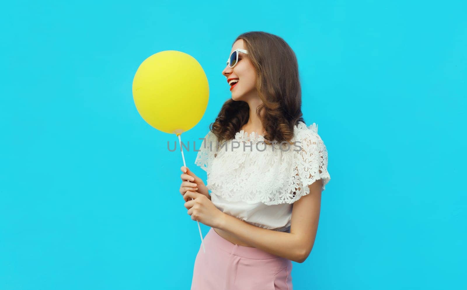 Portrait of happy young woman with yellow balloon on blue studio background