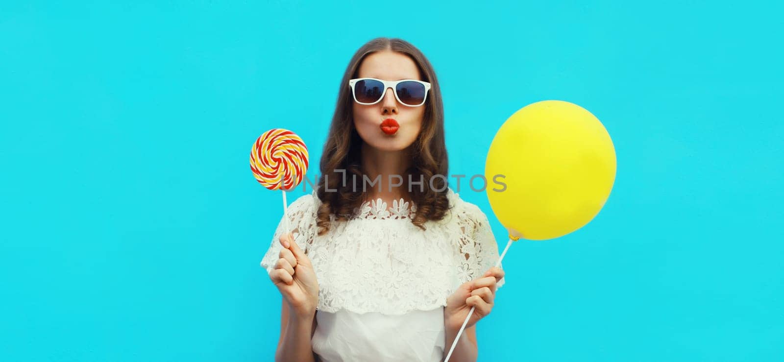 Portrait of happy young woman with yellow balloon on blue studio background