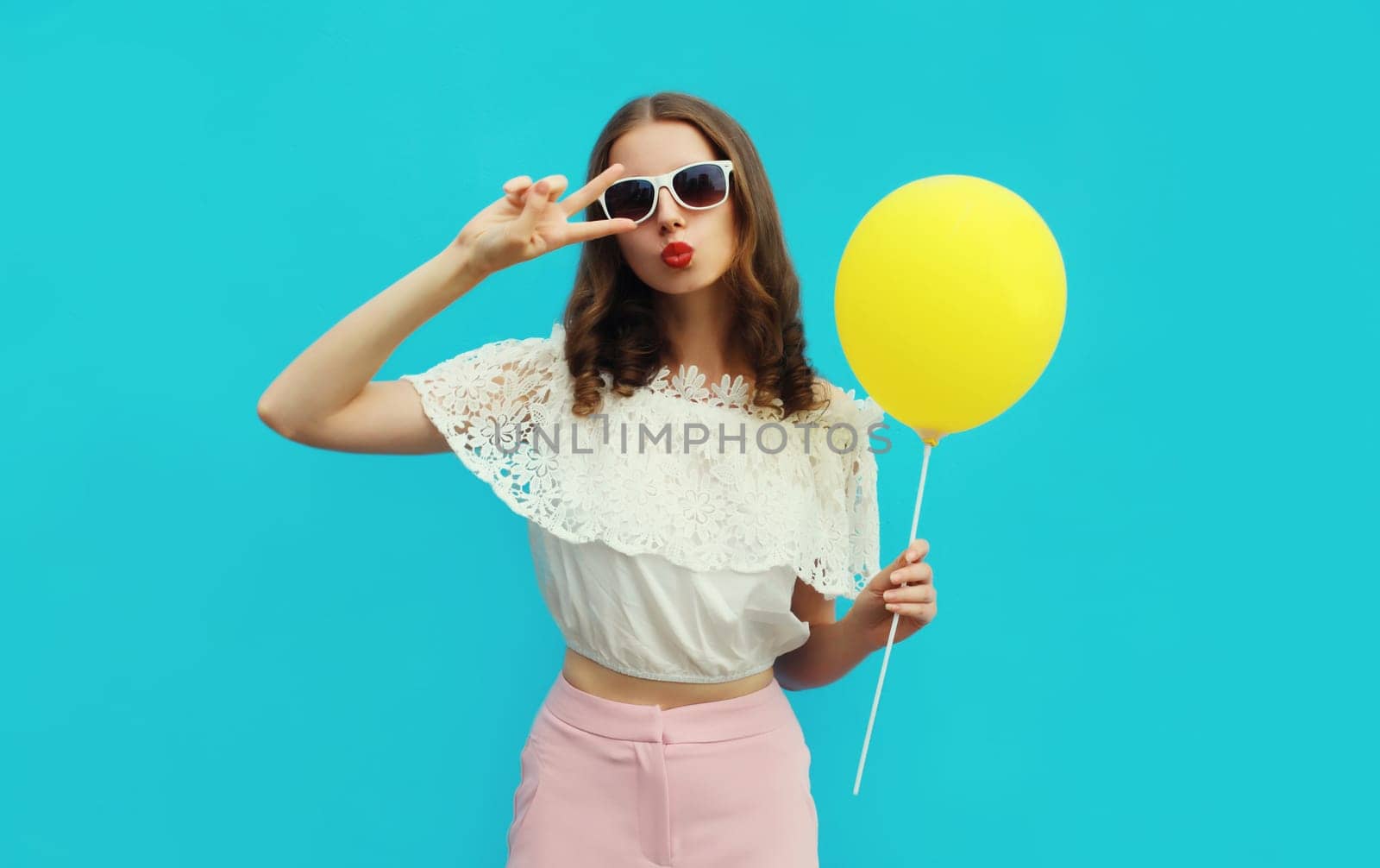 Portrait of happy young woman with yellow balloon on blue studio background