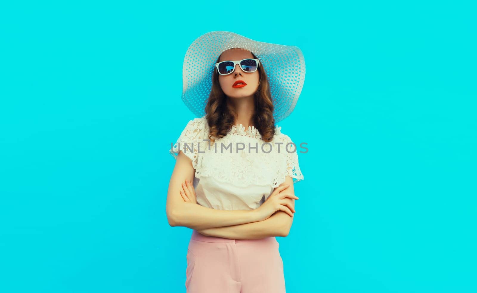 Beautiful caucasian young woman model posing wearing white summer straw hat on blue studio background