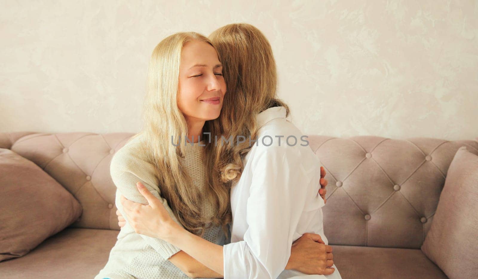 Portrait of happy smiling caucasian middle aged mother hugging her adult daughter together sitting on couch at home